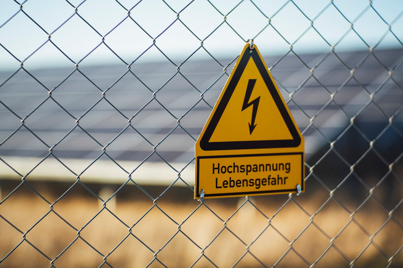 Warning sign indicating high voltage danger on a chain link fence near solar panels.